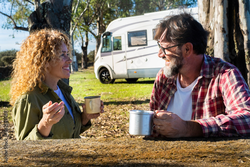 Happy couple of traveler tourist enjoy relax and drinking coffee during travel pause in outdoor at the park with modern rv motorhome vehicle in background under the trees. Autumn journey adventure photo