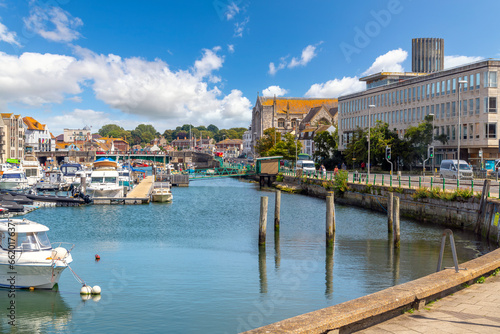 iew of the Weymouth Harbor, with boats docked in the marina, the Town Bridge, and the Holy Trinity St Nicholas Anglican Church, on a sunny summer day in Weymouth, England UK.