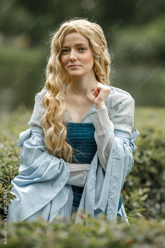 Obraz premium A young beautiful girl in a summer park. A beautiful medieval elf princess in a blue dress in the forest