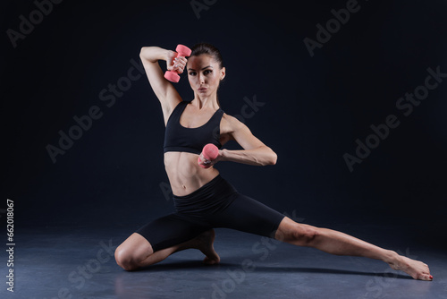 athletic girl in white clothes with dumbbells, on a dark background