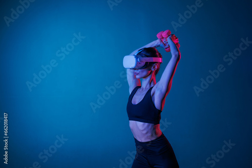 Fototapeta Naklejka Na Ścianę i Meble -  athletic girl doing sports online in VR glasses on a dark background, online sports training