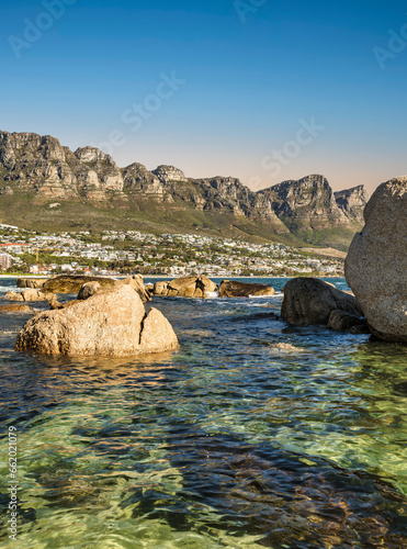 Shot of Camps bay from the Fourth Beach with rocks and atlantic ocean water ribbles during sunset with Twelve Apostles mountain range in the background, Cape Town, South Africa photo