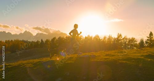 Fototapeta Naklejka Na Ścianę i Meble -  CLOSE UP, LENS FLARE Amazing sunset and lady running on top of hill with her dog