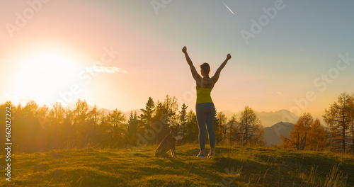 CLOSE UP  LENS FLARE  Woman victoriously raises arms on hilltop in golden light