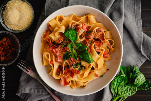 Pappardelle Pasta in Tomato Cream Sauce with Peas and Prosciutto: Italian-style wide noodles in a pasta bowl with basil and grated parmesan cheese
