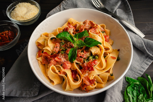 Pappardelle Pasta in Tomato Cream Sauce with Peas and Prosciutto: Italian-style wide noodles in a pasta bowl with basil and grated parmesan cheese
