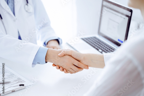Doctor and patient shaking hands while sitting opposite of each other at the table in clinic  just hands close up. Medicine concept