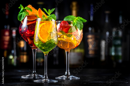 Red, white, pink sangria cocktail drinks with spanish wine, fruits, citrus and ice. Black bar counter background, steel bar tools and bottles