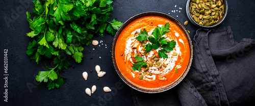 Autumn pumpkin soup puree with pumpkin seeds, cream, pepper and parsley. Winter healthy vegan slow comfort food. Soup bowl on black table background. Top view