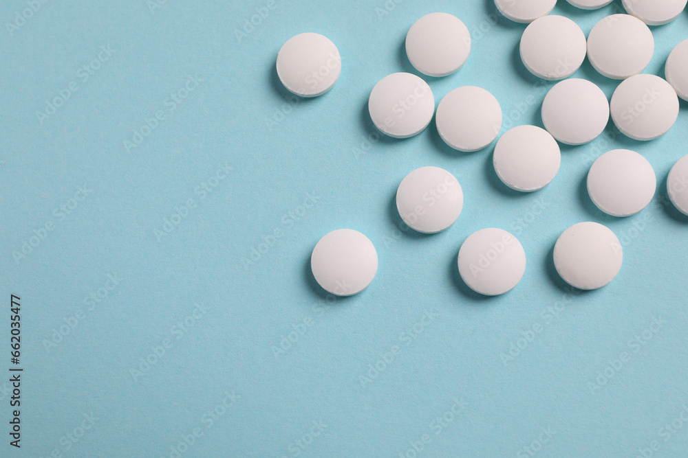 Many white pills on light blue background, flat lay. Space for text