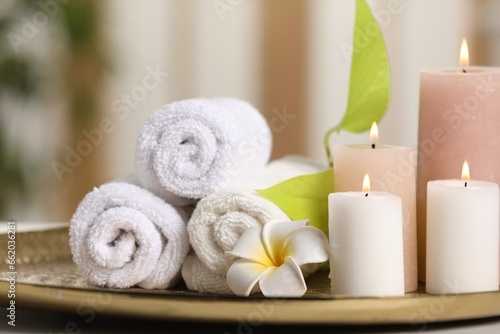 Spa composition. Burning candles, plumeria flower, green leaves and towels on tray, closeup