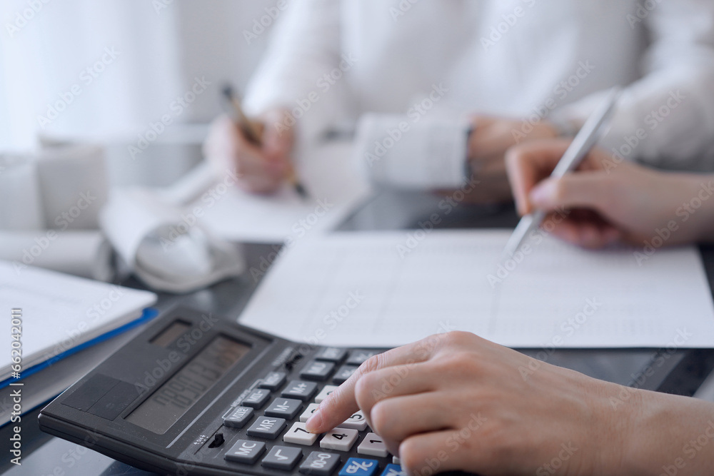 Two accountants use a calculator and laptop computer for counting taxes or revenue balance. Business, audit, and taxes concepts Two accountants use a calculator and laptop computer for counting taxes or revenue balance. Business, audit, and taxes concepts