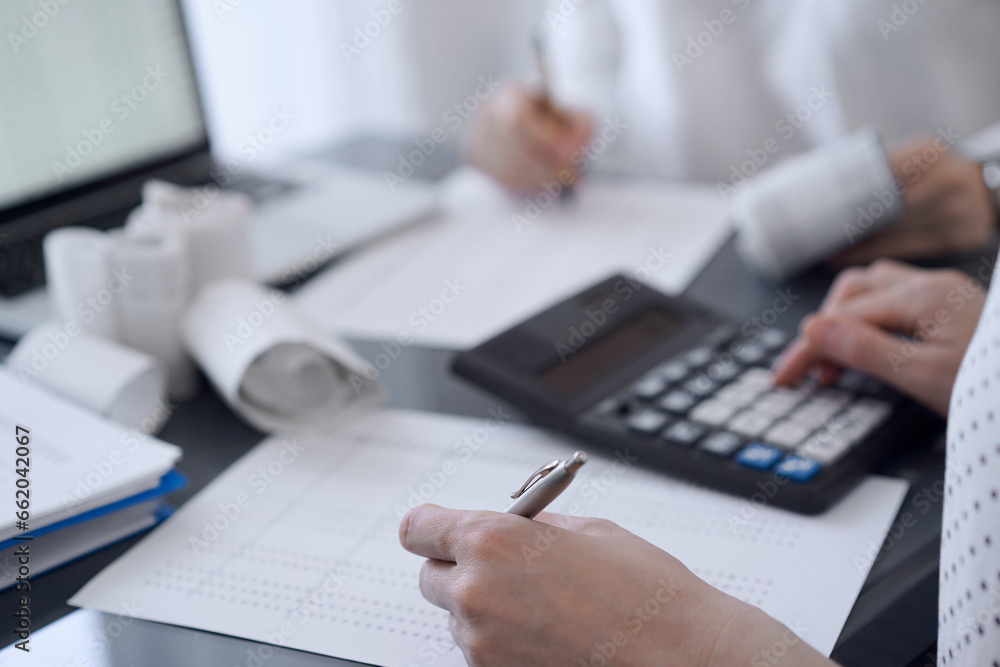 Two accountants use a calculator and laptop computer for counting taxes or revenue balance. Business, audit, and taxes concepts
