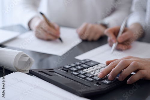 Two accountants use a calculator and laptop computer for counting taxes or revenue balance. Business, audit, and taxes concepts