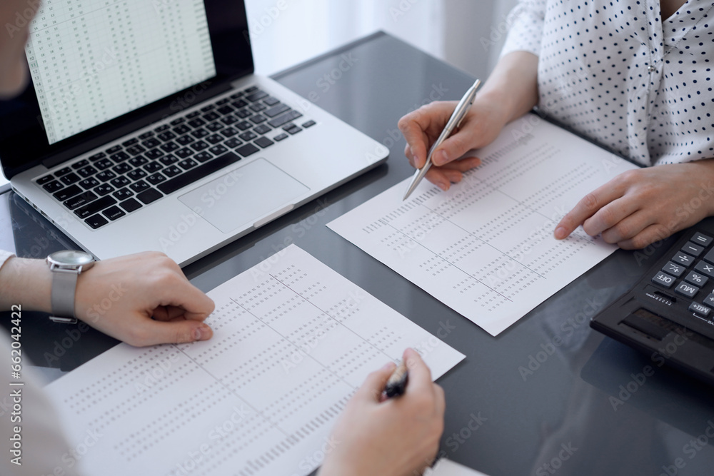 Fototapeta premium Two accountants use a calculator and laptop computer for counting taxes or revenue balance. Business, audit, and taxes concepts