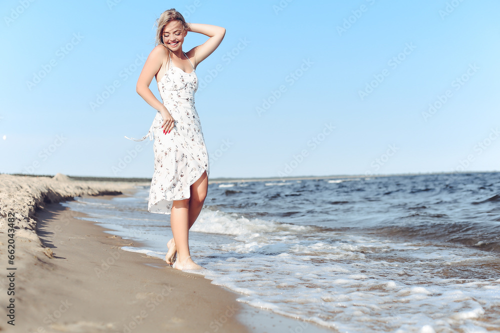 Happy blonde beautiful woman having fun on ocean beach while dancing in waves