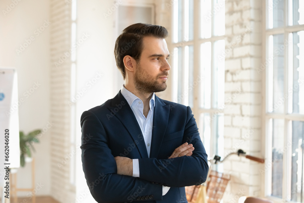 Serious handsome business leader man posing with hands folded in office, looking away in deep thoughts, planning work process, thinking on company future vision, successful ideas Serious handsome business leader man posing with hands folded in office, looking away in deep thoughts, planning work process, thinking on company future vision, successful ideas
