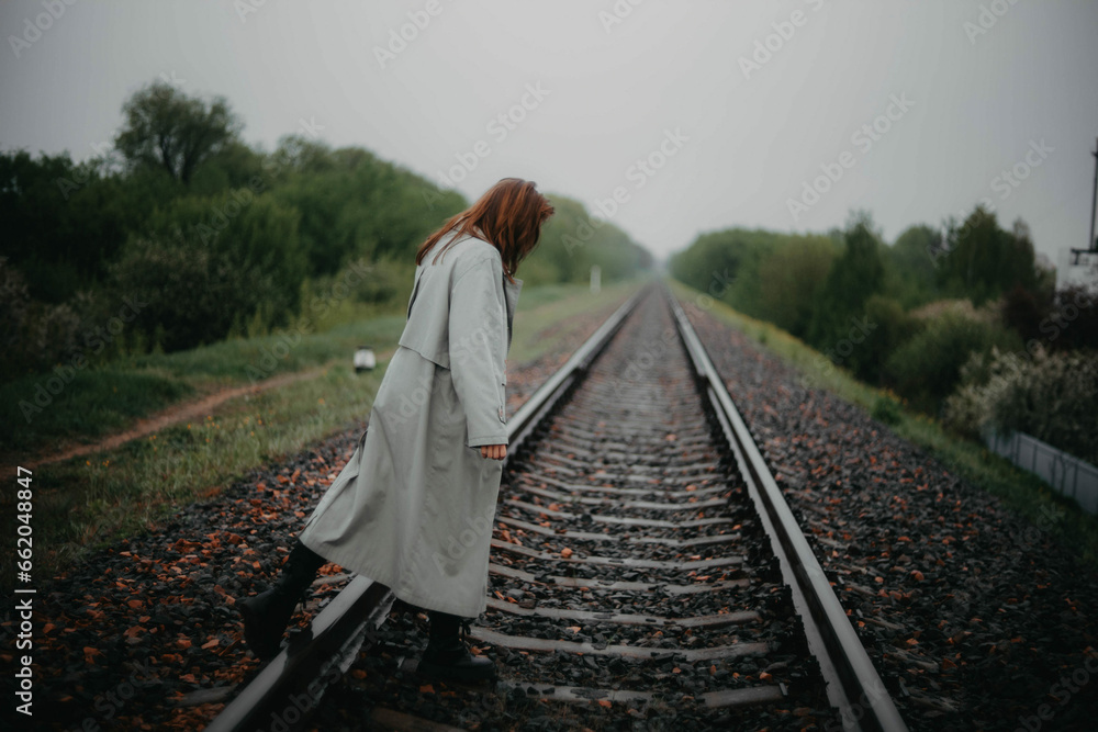 beautiful woman in a gray coat on the railway in gloomy and depressive weather. The concept of loneliness, age crisis, psychological problem.