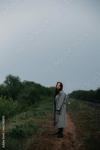 beautiful woman in a gray coat on the railway in gloomy and depressive weather. The concept of loneliness, age crisis, psychological problem. © velimir