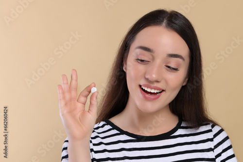 Happy woman showing pill on beige background © New Africa