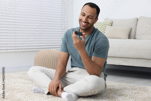 Happy man sending voice message via smartphone indoors