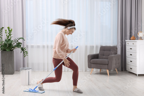 Enjoying cleaning. Happy woman in headphones dancing with mop indoors