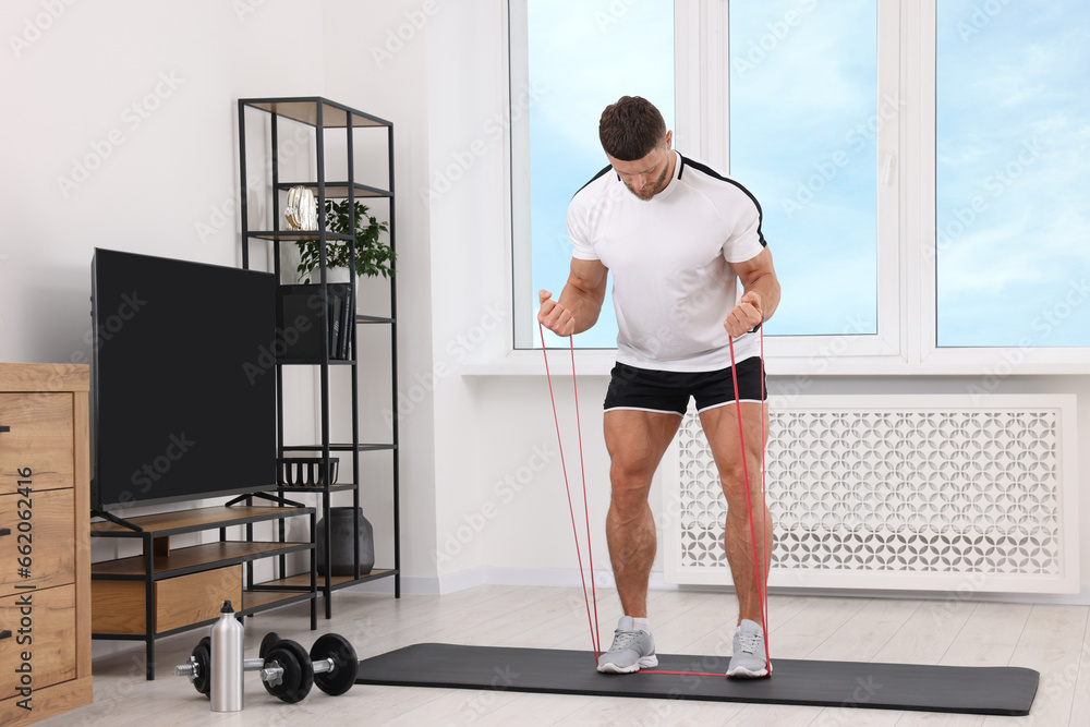 Fototapeta premium Athletic man doing exercise with elastic resistance band on mat at home