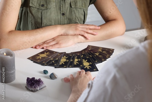 Astrologer predicting client's future with tarot cards at table indoors, closeup photo