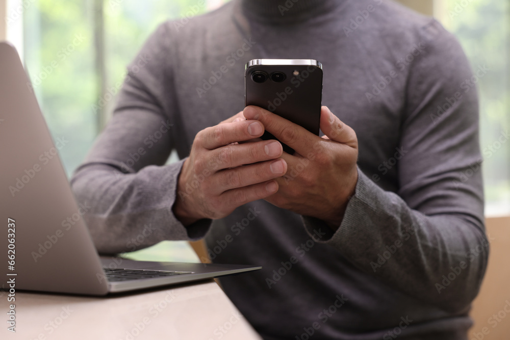 Man sending message via smartphone at table indoors, closeup Man sending message via smartphone at table indoors, closeup