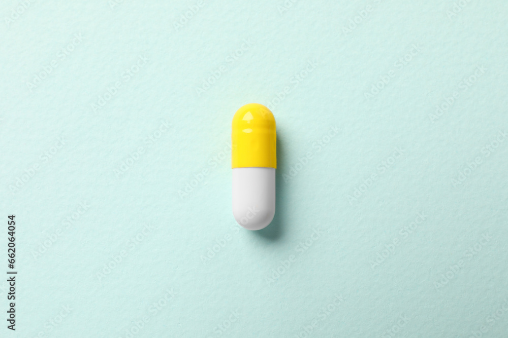 One colorful pill on mint background, top view One colorful pill on mint background, top view