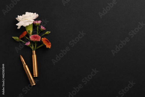 Bullet and cartridge case with beautiful flowers on black background, flat lay. Space for text