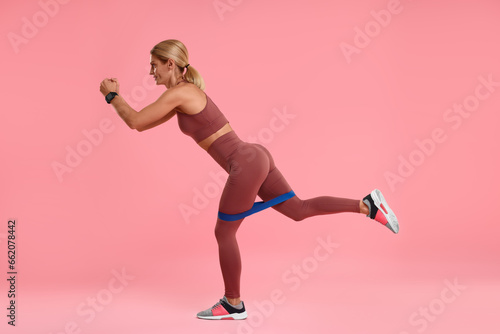 Woman exercising with elastic resistance band on pink background