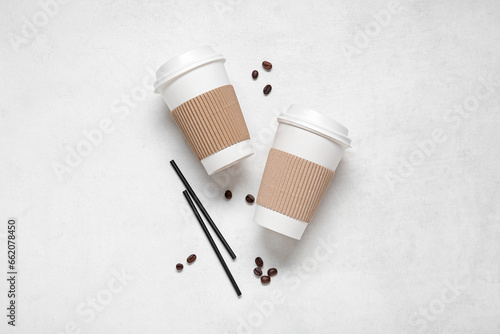 Takeaway paper cups with coffee beans and straws on white background