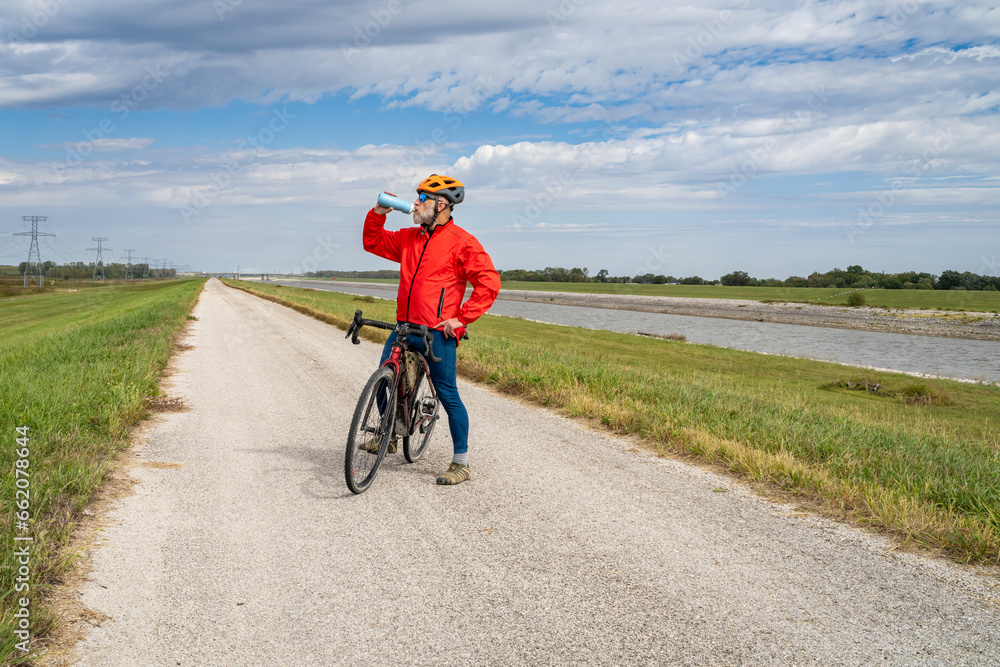 senior athletic man is drinking water during biking a gravel touring bike on a levee trail along Chain of Rocks Canal near Granite City in Illinois