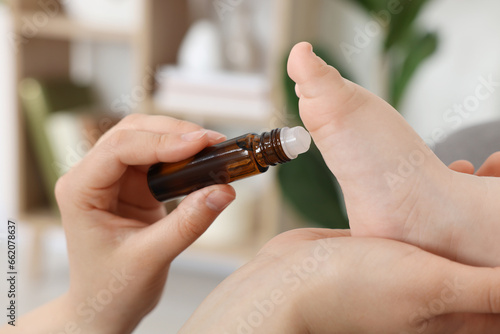Mother applying essential oil from roller bottle onto her baby s heel indoors  closeup