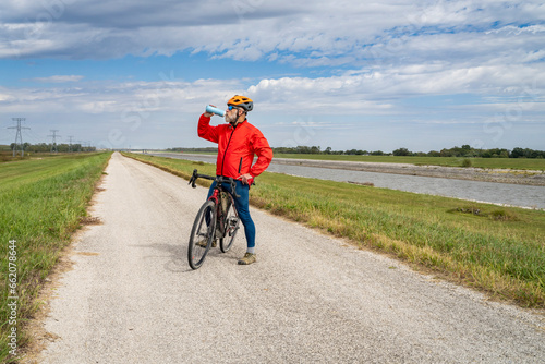 senior athletic man is drinking water during biking a gravel touring bike on a levee trail along Chain of Rocks Canal near Granite City in Illinois