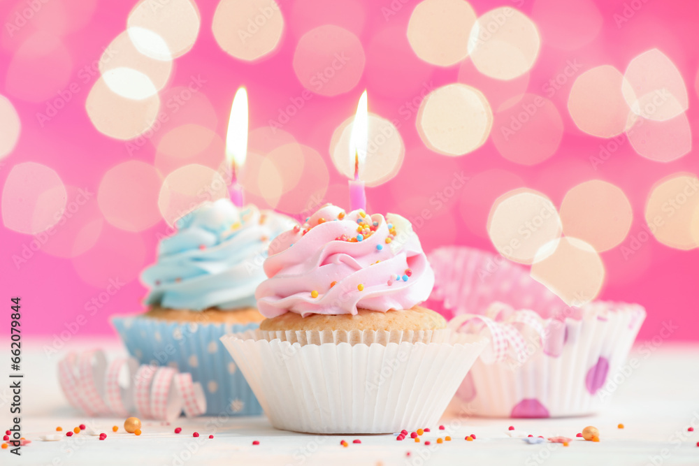 Tasty Birthday cupcakes with burning candles on table against blurred lights Tasty Birthday cupcakes with burning candles on table against blurred lights