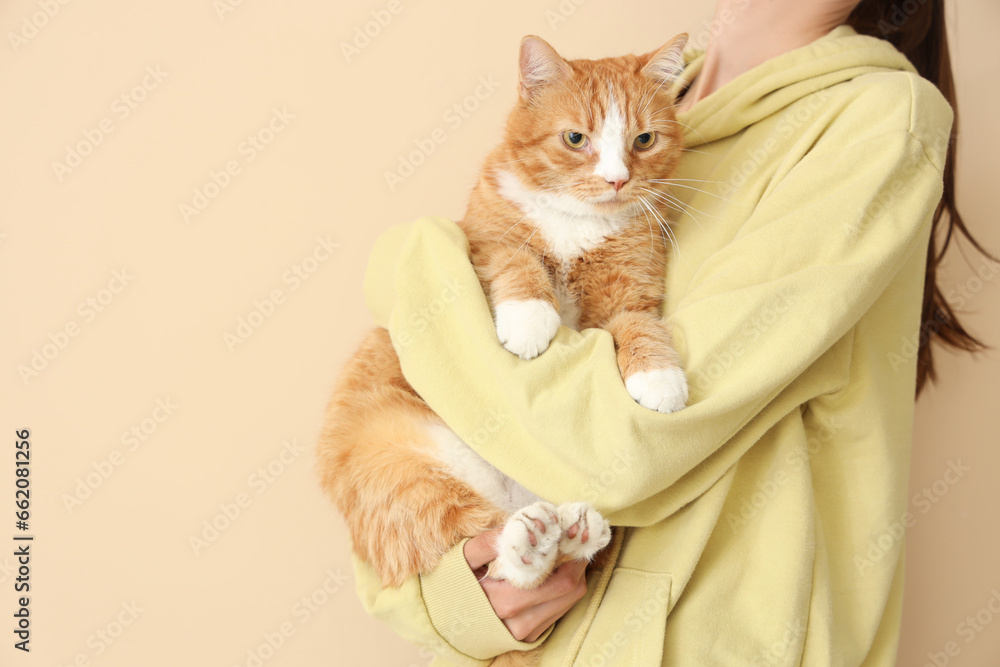 Woman with cute red cat on beige background, closeup
