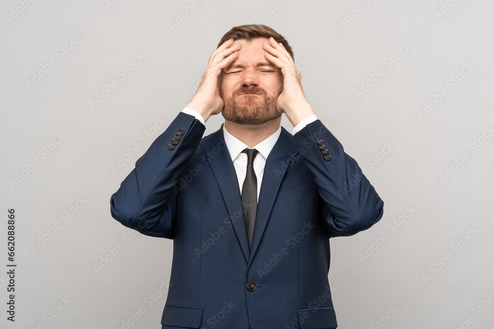 Man touching head, frown disappointed sickly emotional face with closed eyes on grey background. Businessman having problems troubles in business. Losing money, burnout, desperation, failure concept. Man touching head, frown disappointed sickly emotional face with closed eyes on grey background. Businessman having problems troubles in business. Losing money, burnout, desperation, failure concept.