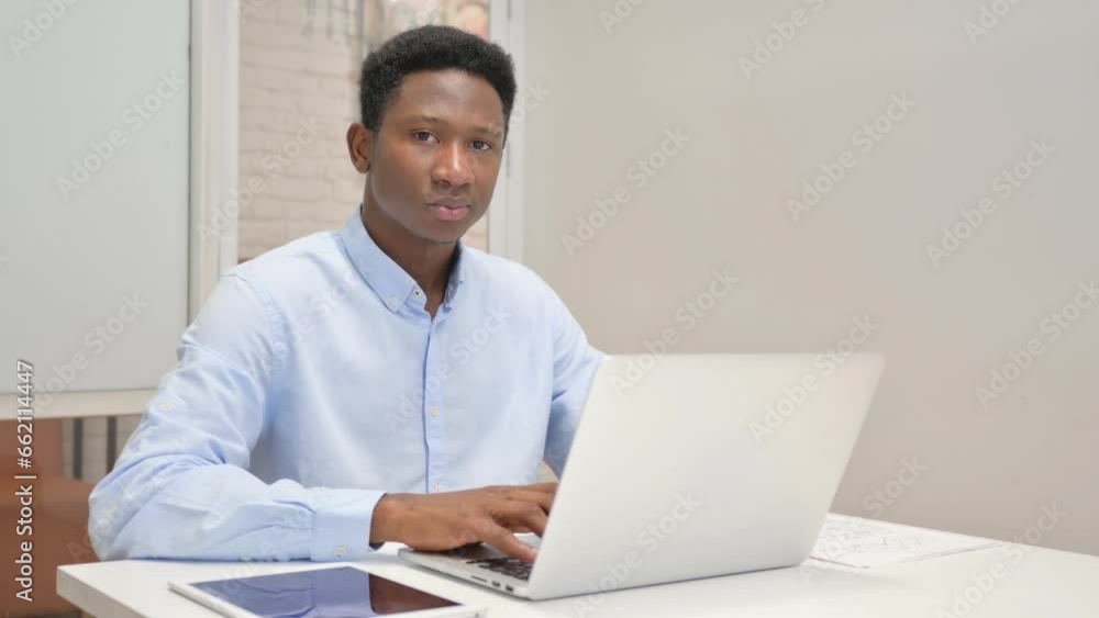 African Businessman Looking at Camera while Working on Laptop in Office African Businessman Looking at Camera while Working on Laptop in Office