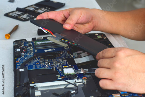 computer technician laptop motherboard repair technician Removing the battery from the notebook computer photo