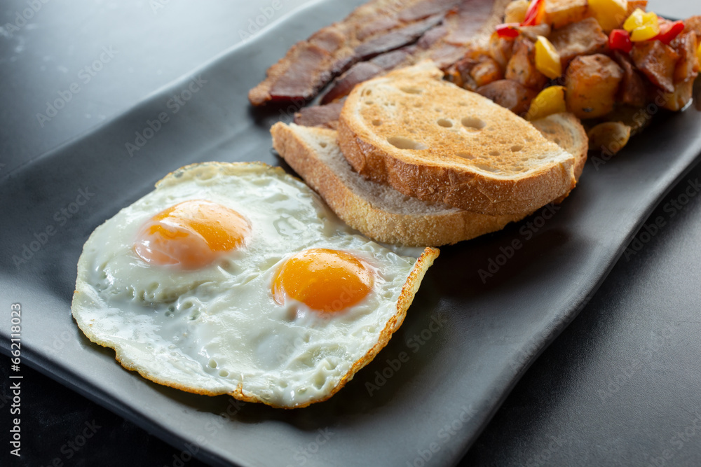 A view of a breakfast plate, featuring eggs, toast, bacon and potatoes. A view of a breakfast plate, featuring eggs, toast, bacon and potatoes.