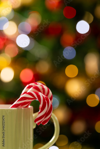 Vertical image of mug with candy canes and christmas tree with fairy lights and copy space