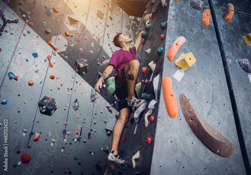 A strong male climber climbs an artificial wall with colorful grips and ropes.