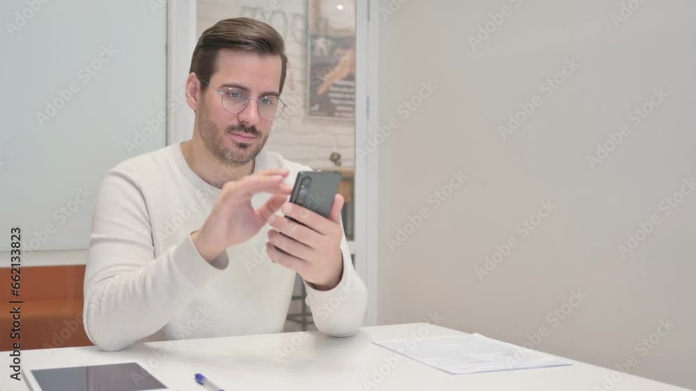 Young Man Browsing Internet on Phone in Office
