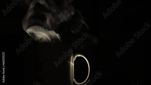A cup of coffee on a black background, illuminated by light from behind. Silhouetted at night, the coffee is clearly visible as steam comes out of it. Making espresso, time for a break. photo