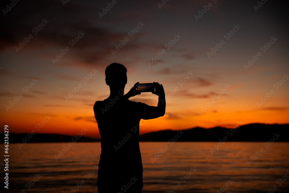 silhouette of a man taking a photo of a sunset over the sea