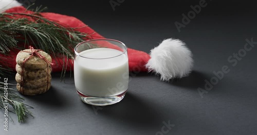 Video of christma cookies, glass of miljk, santa clasus hat and copy space on black background photo