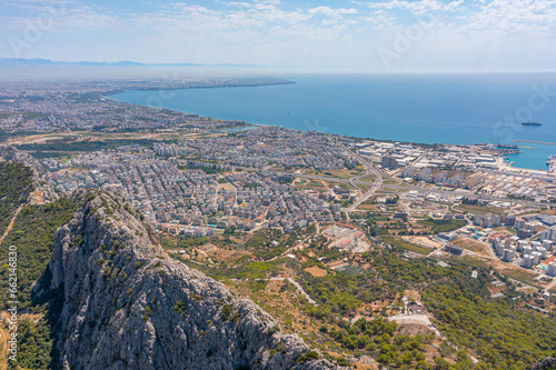 Flight over ridge mountain pass rocky terrain with bushes, bird's eye view overlooking the city, houses and buildings, roads and ships, Mediterranean coast, resort area, vacation trip. © aapsky
