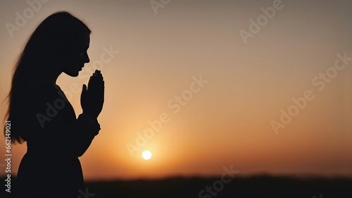 Silhouette of a praying girl with folded palms at sunset photo